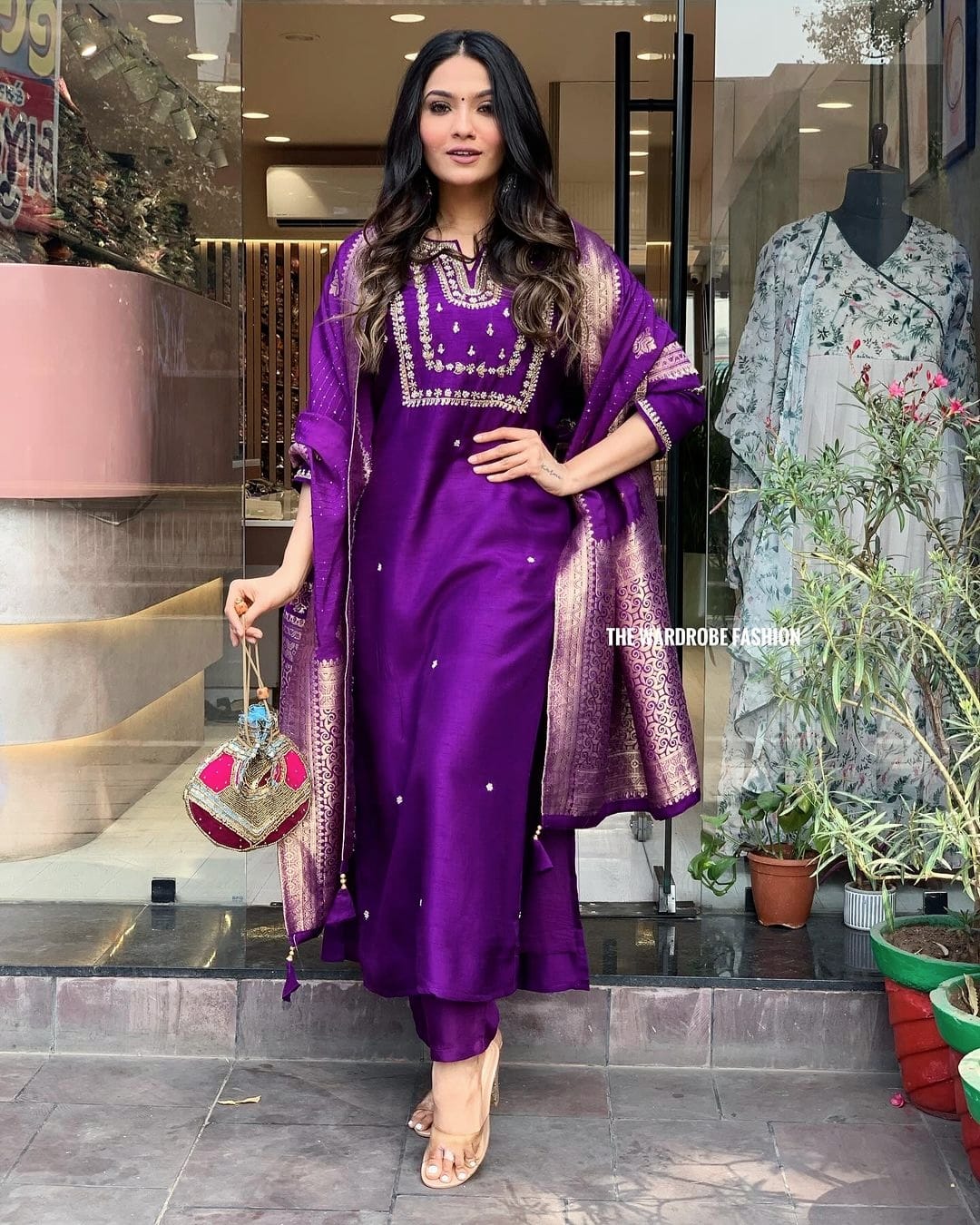 Woman in a purple traditional outfit standing in front of a store entrance.